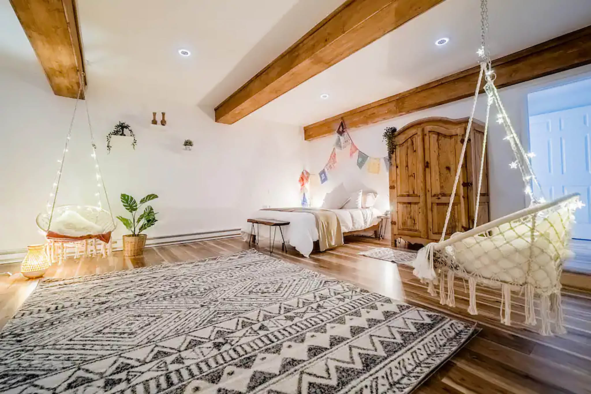 A bright studio with exposed wood beams, a bed, and woven chairs.