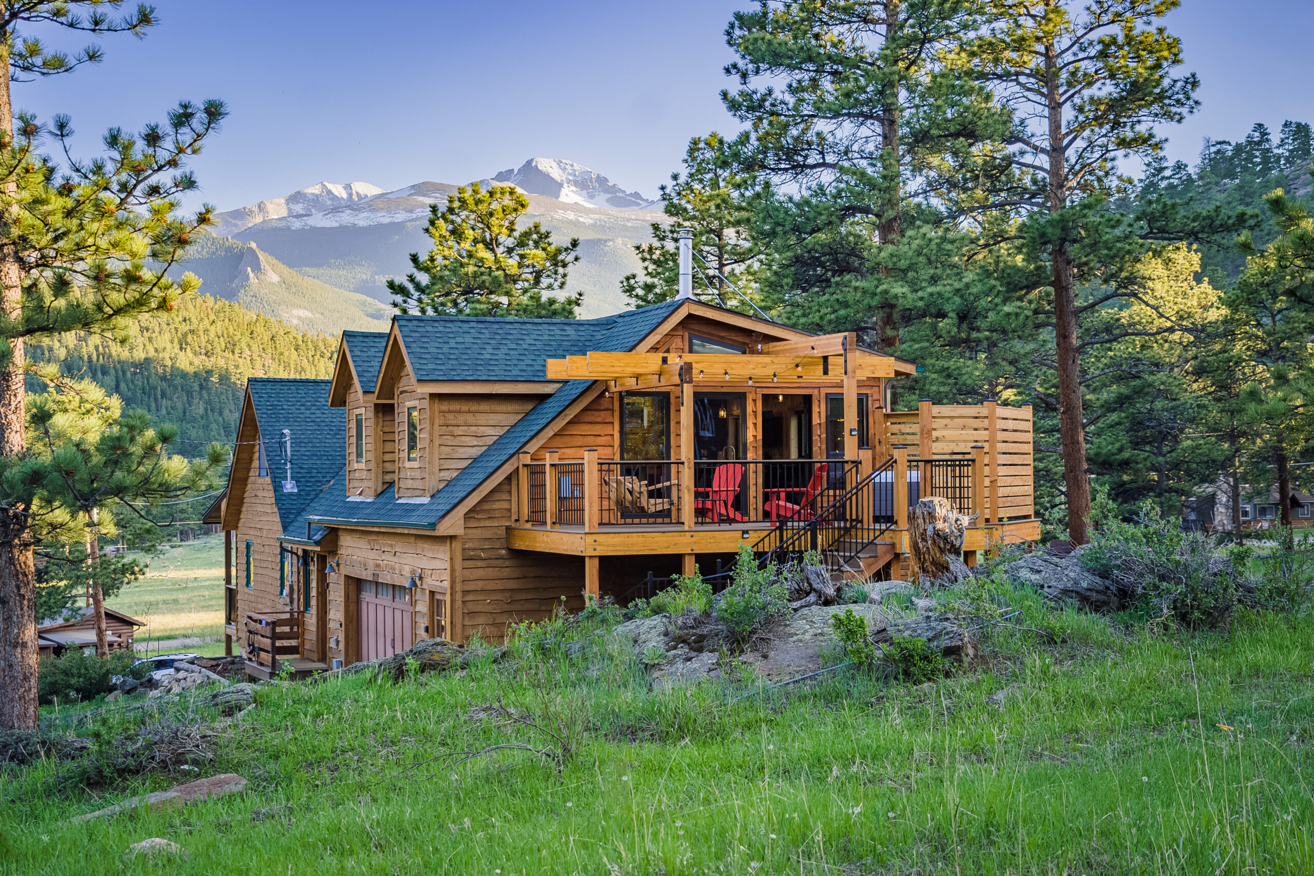 A timber-sided mountain home beneath snow-capped peaks, surrounded by pines.