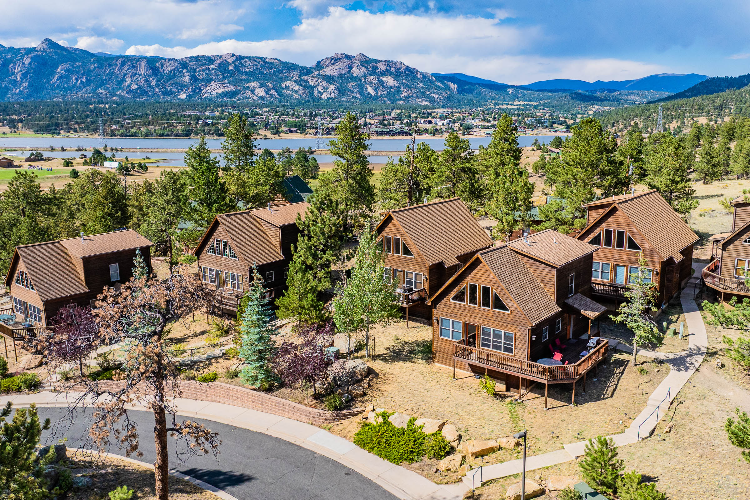 A group of timber cabins among pines, with Lake Estes and mountains beyond.